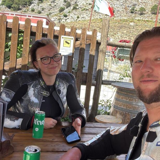 Ein Mann und eine Frau in Biker-Kleidung sitzen an einem Tisch und machen ein Selfie.