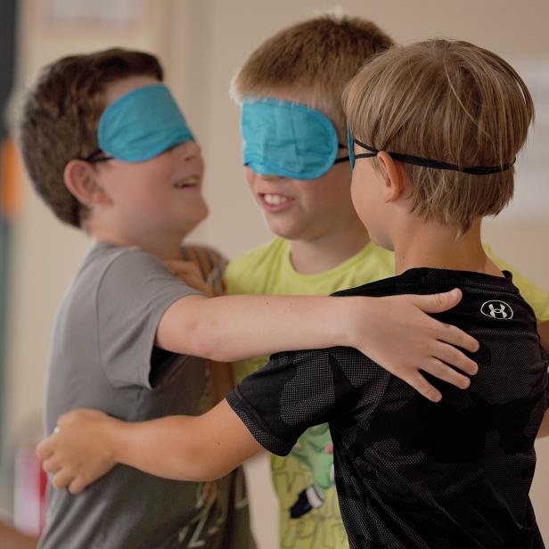 Drei Kinder mit Augenbinden umarmen sich und lächeln dabei.