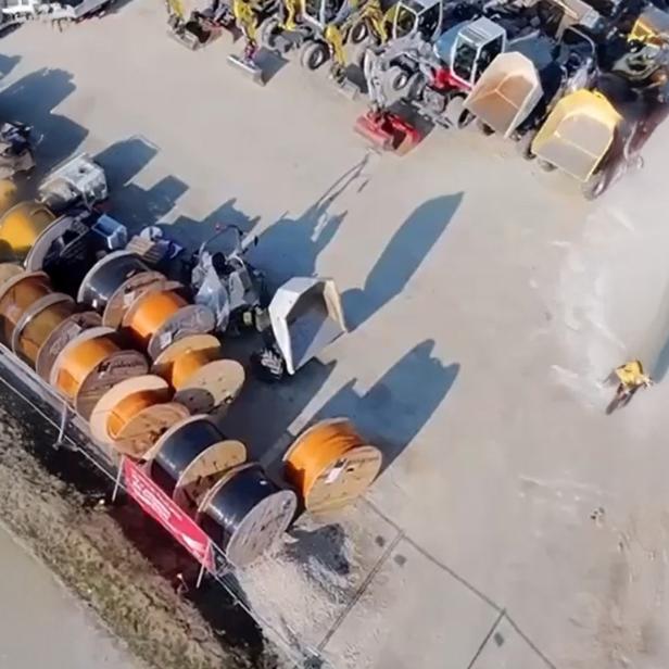 Große Kabeltrommeln und Baumaschinen auf einem Baustellenlagerplatz aus der Vogelperspektive.