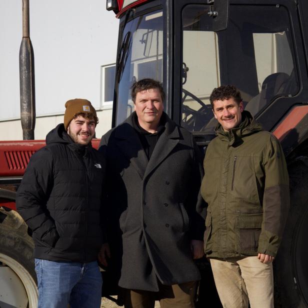 Drei Männer stehen vor einem roten Traktor auf einem Feld.