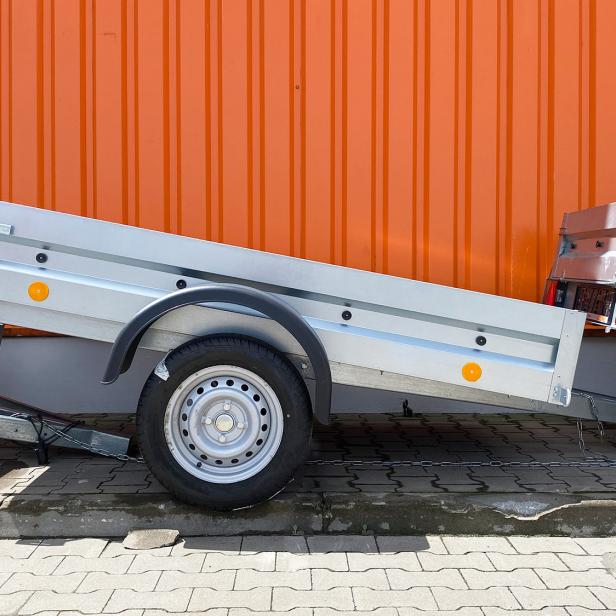 Mehrere Autoanhänger stehen vor einem orangen Container.