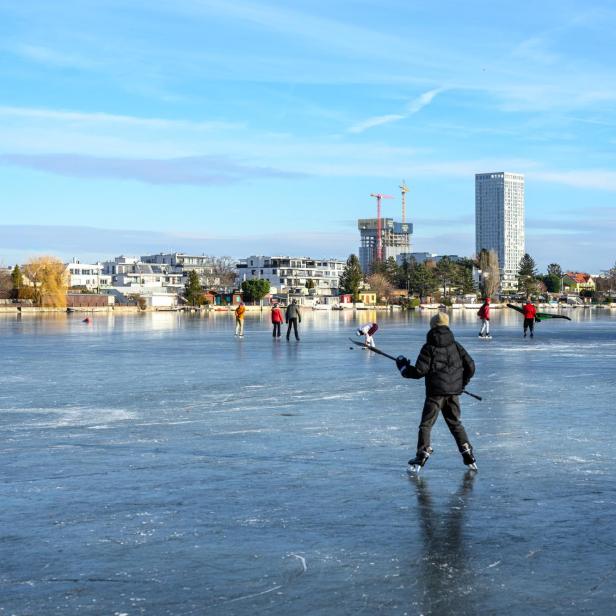 Mehrere Menschen spielen Eishockey und laufen Schlittschuh auf der zugefrorenen Alten Donau