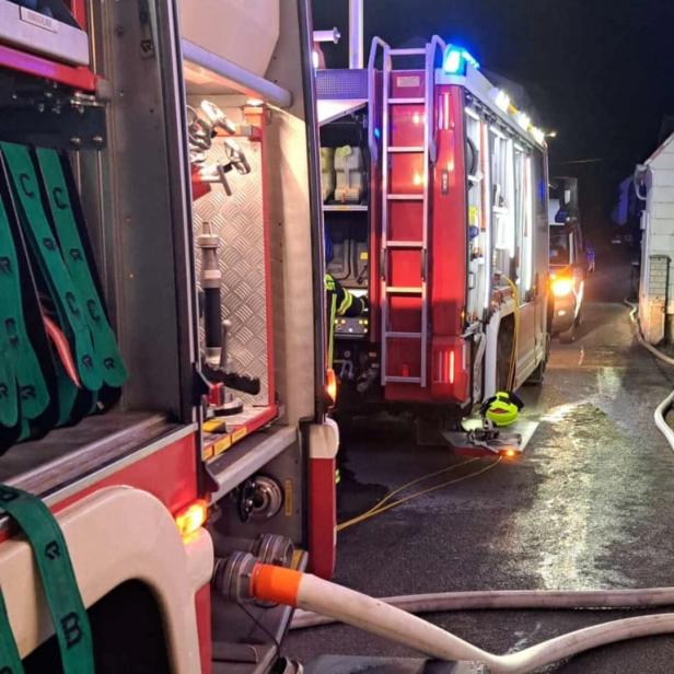 Zwei Feuerwehrfahrzeuge mit angeschlossenen Schläuchen und Ausrüstung stehen nachts auf einer nassen Straße.
