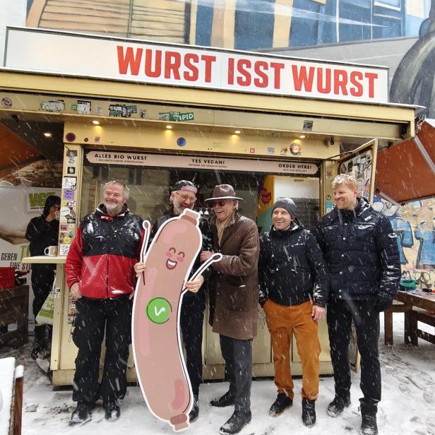 Mehrere Menschen stehen vor dem Würstelstand mit Aufschrift "Wurst isst Wurst"