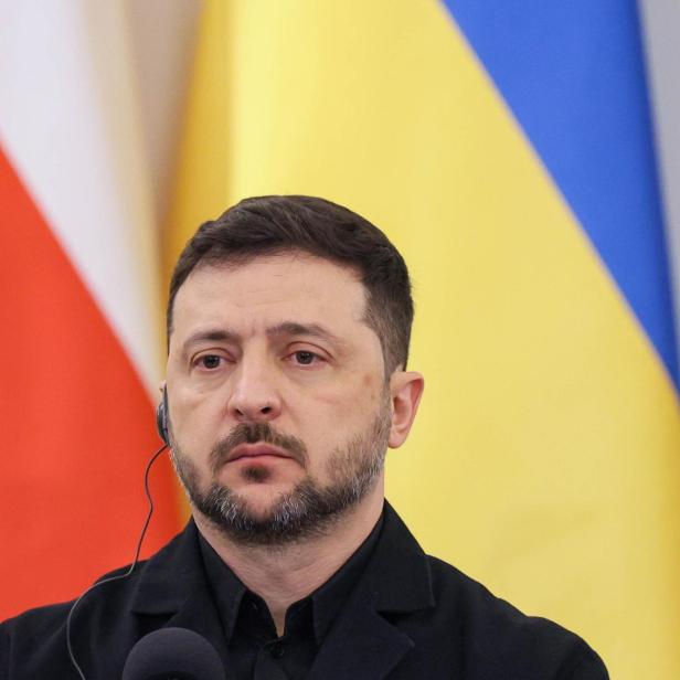 Wolodymyr Selenskyj mit Headset vor den Flaggen der Ukraine und Polens.