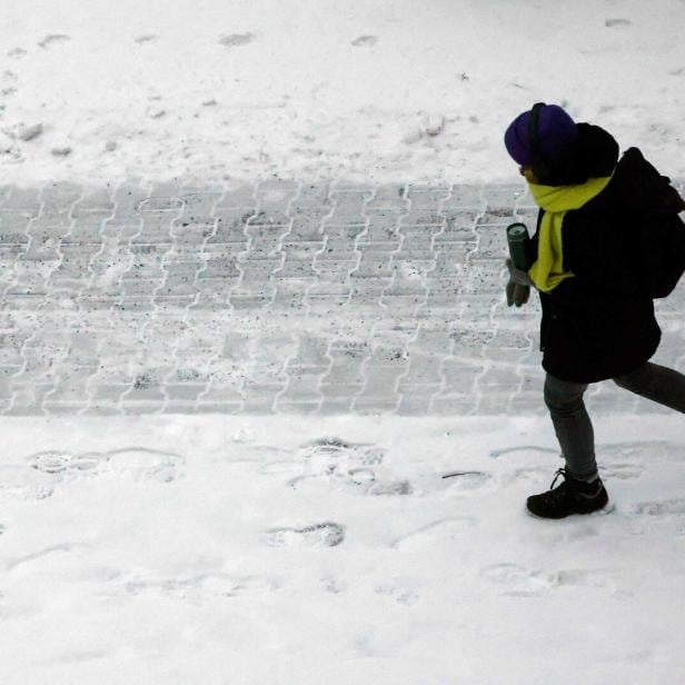 Ein Mensch geht auf einer winterlichen, teils mit Schnee bedeckten Straße.