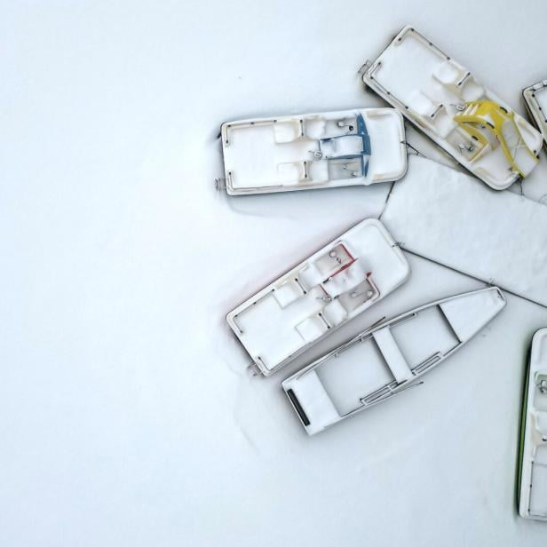 Mehrere schneebedeckte Boote in verschiedenen Farben liegen auf einer weißen Oberfläche.