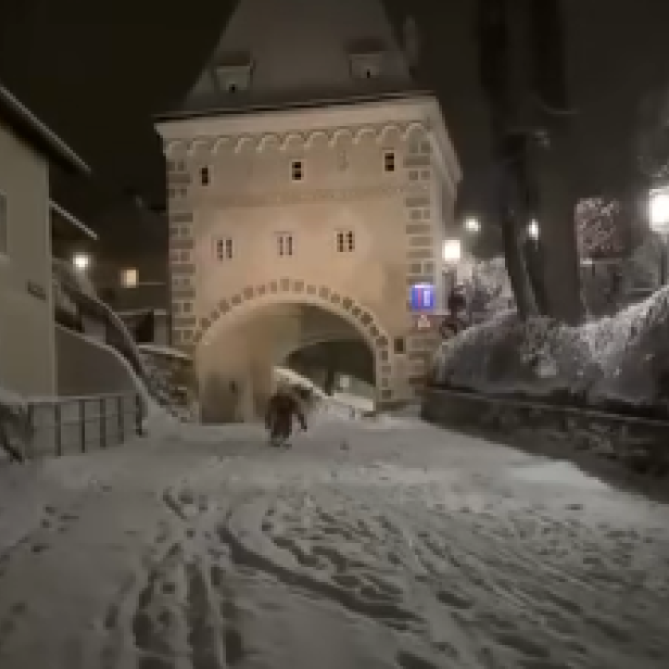 Ein Skifahrer fährt nachts durch die verschneite Altstadt von Steyr beim Schnallentor.
