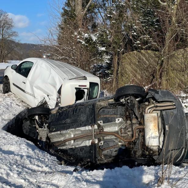 Zwei beschädigte Fahrzeuge liegen im verschneiten Straßengraben, ein Rettungswagen steht daneben.