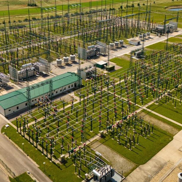 Große Umspannanlage mit zahlreichen Stromleitungen, Transformatoren und Gebäuden auf grünem Gelände.