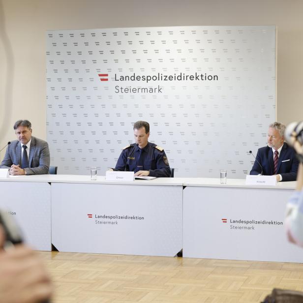 Drei Männer sitzen bei einer Pressekonferenz der Landespolizeidirektion Steiermark an einem Tisch, eine Frau fotografiert sie.