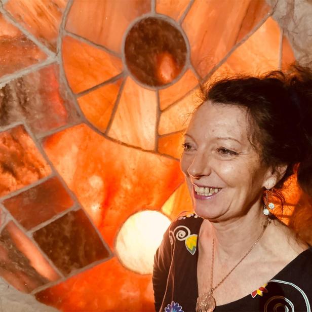 Eine Frau mit lockigen, roten Haaren vor orangenem Glasfenster 