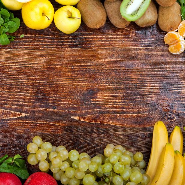Verschiedene frische Obstsorten wie Äpfel, Bananen, Trauben und Zitrusfrüchte auf Holztisch.
