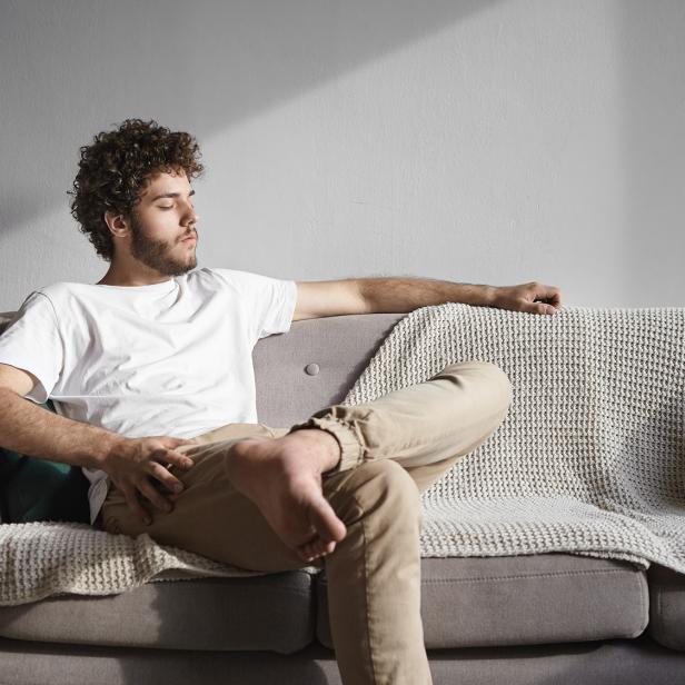 Mann entspannt barfuß auf einem Sofa im hellen, gemütlichen Wohnzimmer.