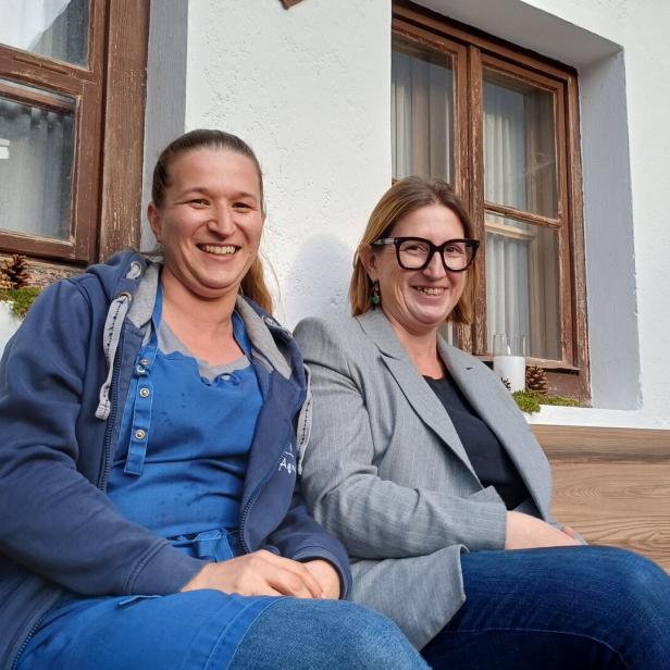 Die Almwirtinnen Agi und Michi sitzen auf einer Bank vor ihrem Gasthaus. 
