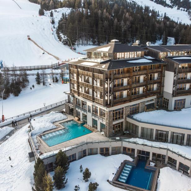 Hotel mit Außenpool direkt an einer verschneiten Skipiste in alpiner Winterlandschaft.