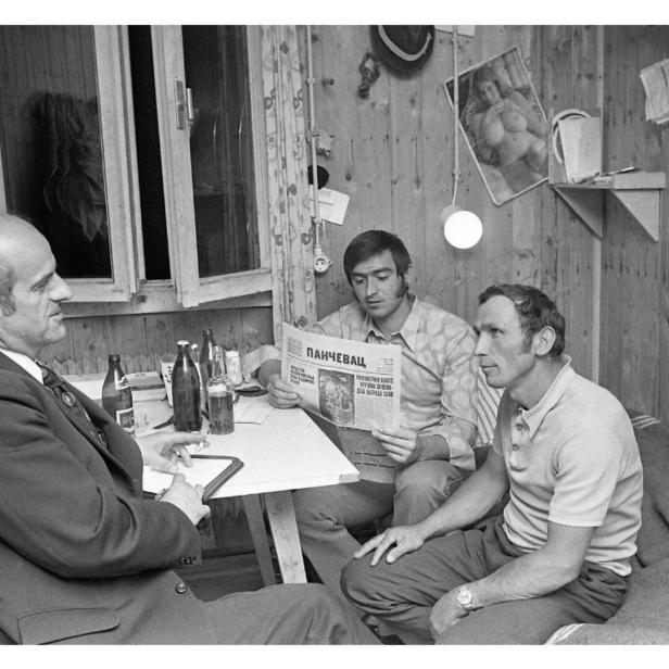 Drei Männer sitzen um einen Tisch in einer Arbeiterunterkunft.