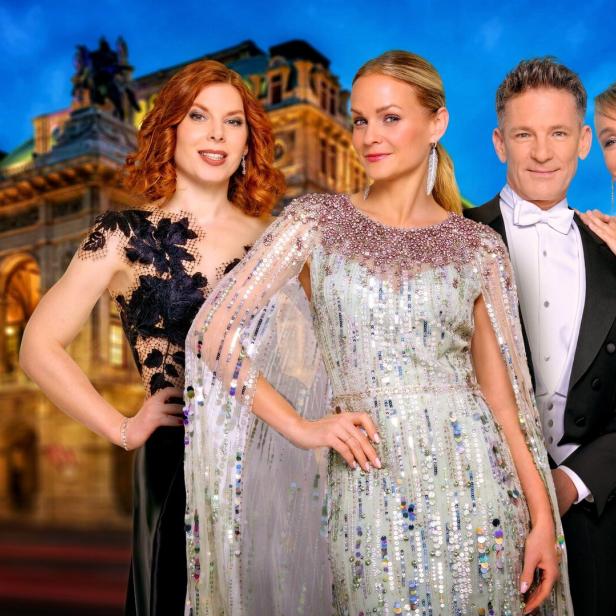 Vier elegant gekleidete Personen posieren vor einem beleuchteten historischen Gebäude am Abend.