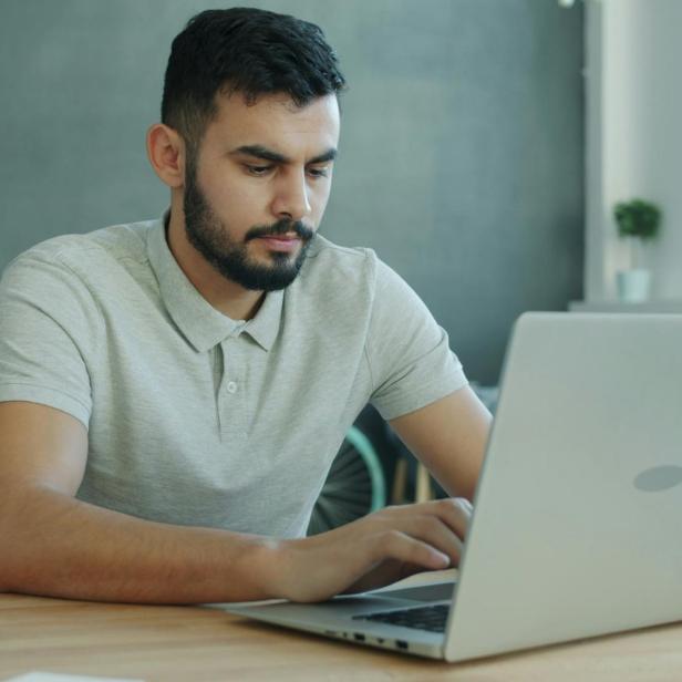 Ein Mann sitzt an einem Schreibtisch in einem Büro und arbeitet an einem Laptop.