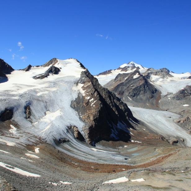 Eine Berglandschaft mit schneebedeckten Gipfeln und einem Gletscher unter blauem Himmel.