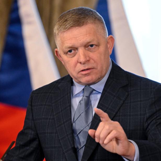 Ein Mann im Anzug gestikuliert vor Flaggen.