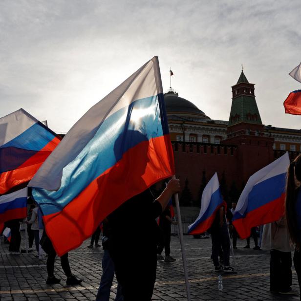 Menschen halten russische Flaggen vor dem Hintergrund des Moskauer Kremls.