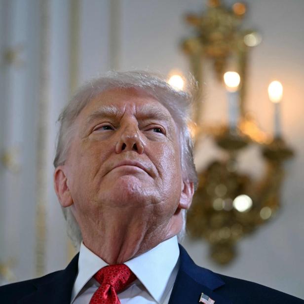 Donald Trump blickt mit roter Krawatte und Anstecknadel der US-Flagge nach oben.