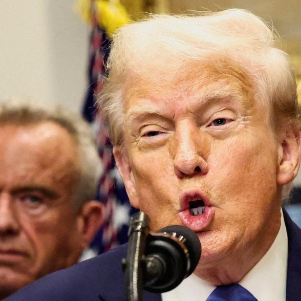 Donald Trump spricht am Mikrofon, eine weitere Person ist im Hintergrund zu sehen.