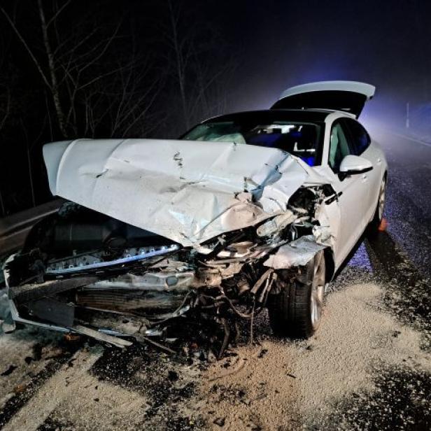 Stark beschädigtes weißes Auto nach Frontalzusammenstoß auf winterlicher Landstraße.
