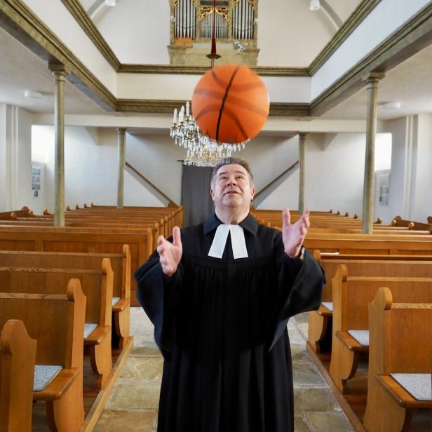 Ein Pfarrer jongliert in einer Kirche mit einem Basketball.