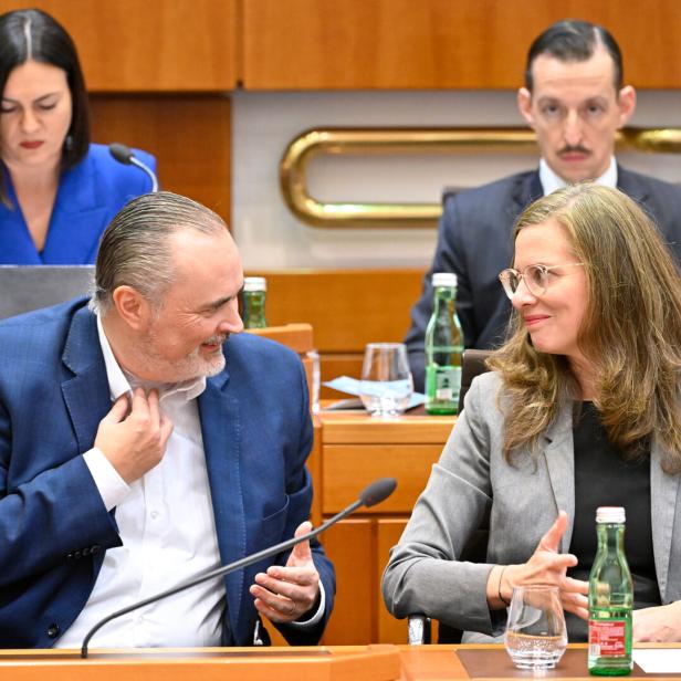 Zwei Personen im Anzug unterhalten sich freundlich an einem Konferenztisch, im Hintergrund sitzen weitere Menschen.