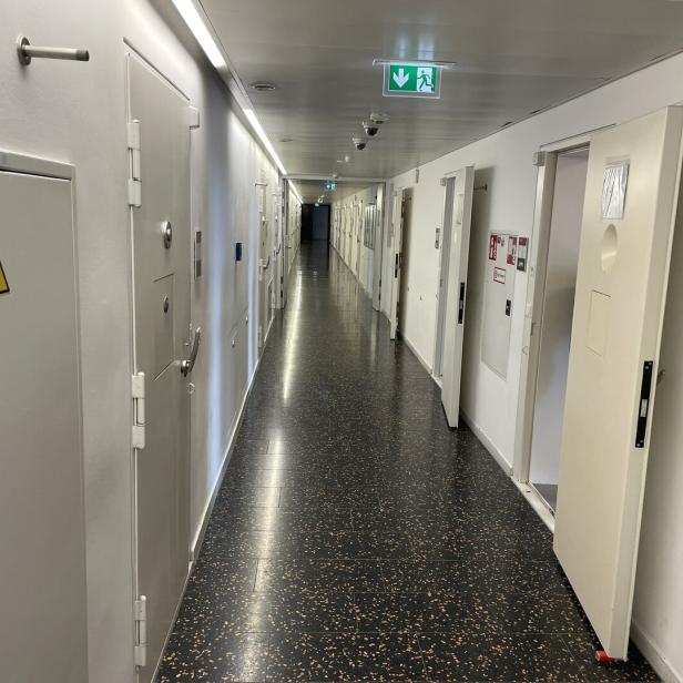 Ein langer Flur mit weißen Türen und einem Notausgangsschild erstreckt sich in die Ferne.