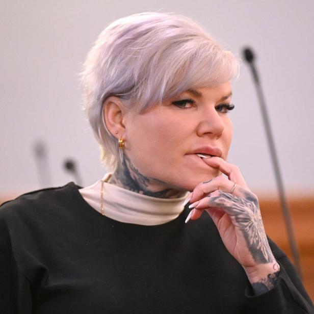 Melanie Müller mit kurzen, hellen Haaren und sichtbaren Tattoos am Hals und an der Hand blickt nachdenklich zur Seite.