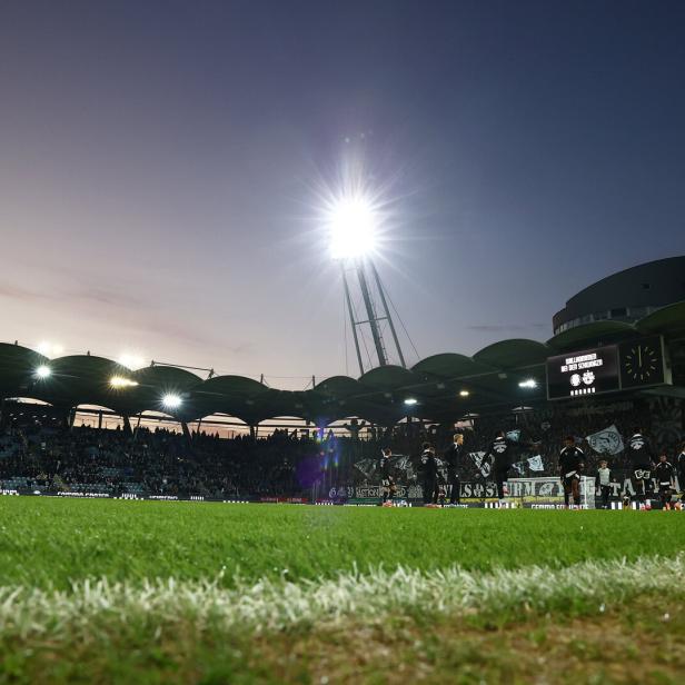 Ein Fußballstadion mit Zuschauern und Flutlicht unter einem Abendhimmel.