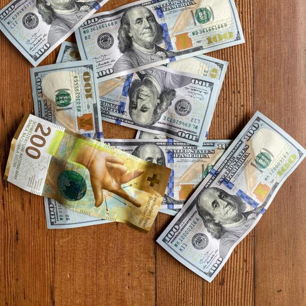 Mehrere 100-Dollar-Scheine und ein 200-Franken-Schein auf Holztisch.
