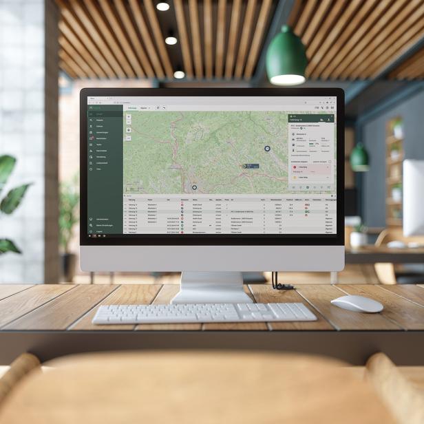 Monitor mit Fuhrparkmanagement-Software und Kartenansicht in modernem Büro mit Pflanzen.