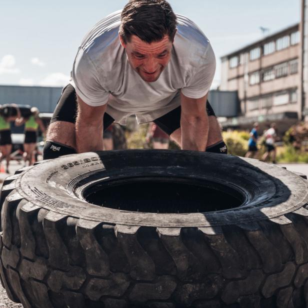 Mann hebt im Freien einen großen Traktorreifen bei einem Fitness-Training an.