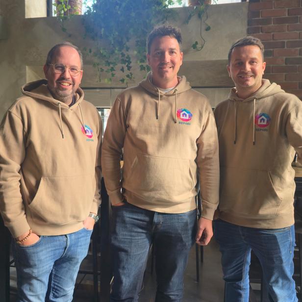 Drei Männer stehen in beigen Hoodies nebeneinander 