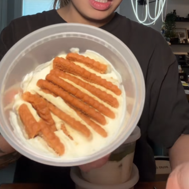 Frau hält Joghurtbecher mit Joghurt und Keksen in die Kamera