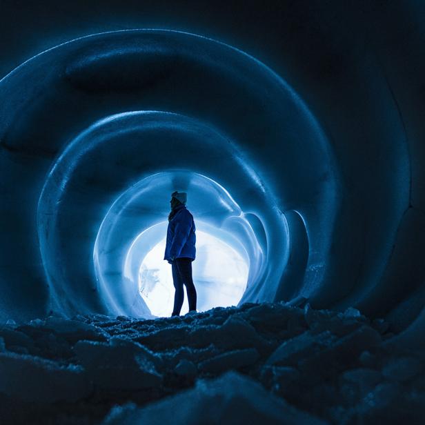 Person steht in einer blau beleuchteten Eishöhle mit spiralförmigen Wänden.