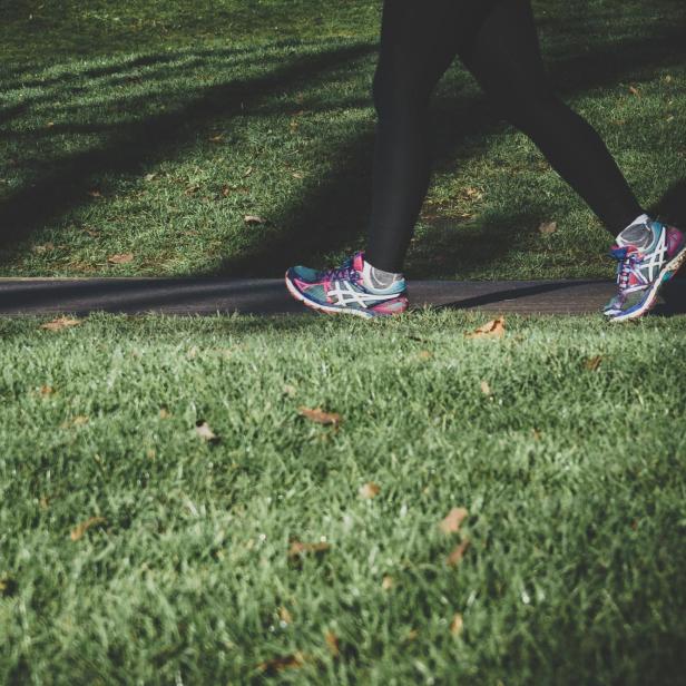 Frau in Turnschuhen geht inmitten einer Grünfläche walken