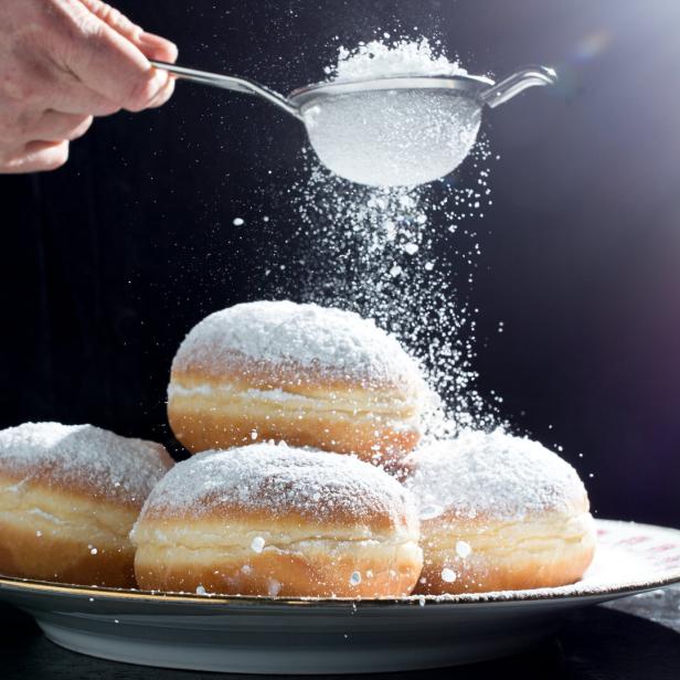 Ein Teller Krapfen wird mit Puderzucker bestreut.