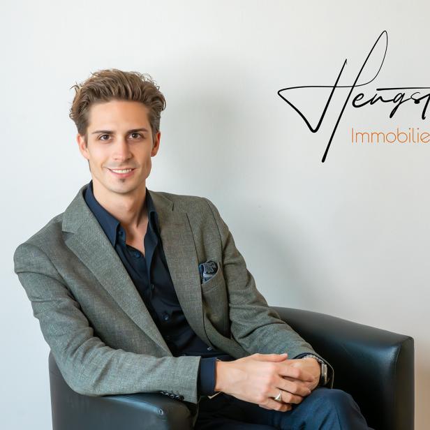 Ein Mann im Anzug sitzt auf einem schwarzen Sessel. 