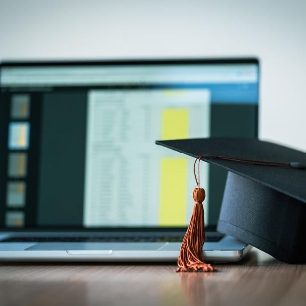 Ein Laptop steht auf einem Tisch, daneben liegt ein schwarzer Doktorhut mit Quaste.