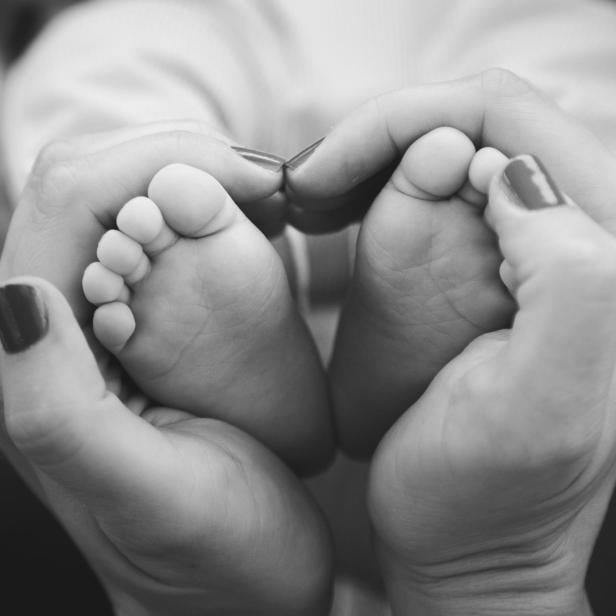 Schwarzweißfoto einer Frauenhand, die Babyfüße in Händen hält