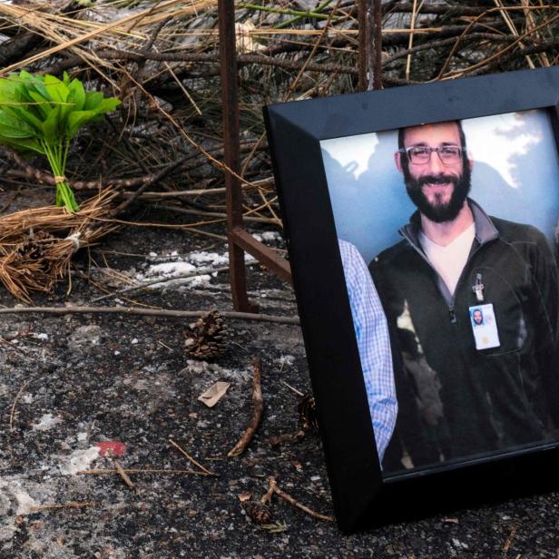 Ein gerahmtes Porträt eines Mannes mit Bart liegt neben Blumen und einer Kerze auf dem Boden.