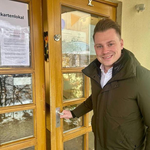 Ein Mann in Jacke öffnet die Tür zu einem Wahllokal, an der Aushänge befestigt sind.