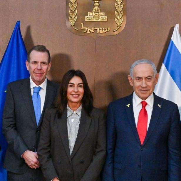 Drei Personen posieren vor Flaggen und dem Staatswappen Israels, darunter Benjamin Netanjahu mit roter Krawatte.