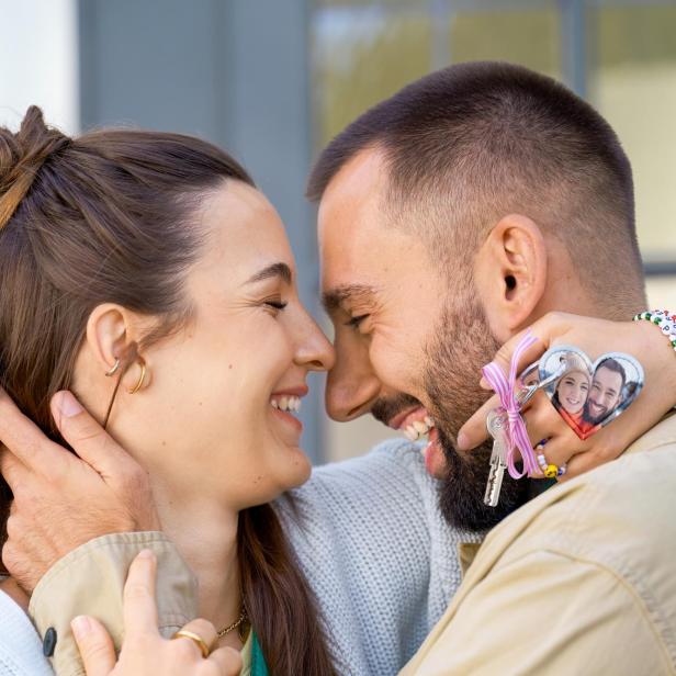Ein Paar lächelt sich an, sie hält einen herzförmigen Schlüsselanhänger mit Foto.