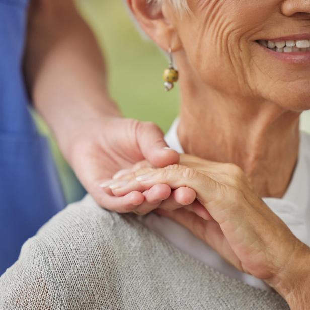 Eine ältere Frau wird von einer Pflegekraft fürsorglich an der Hand gehalten.